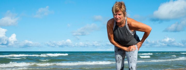 woman holding hip on beach during run