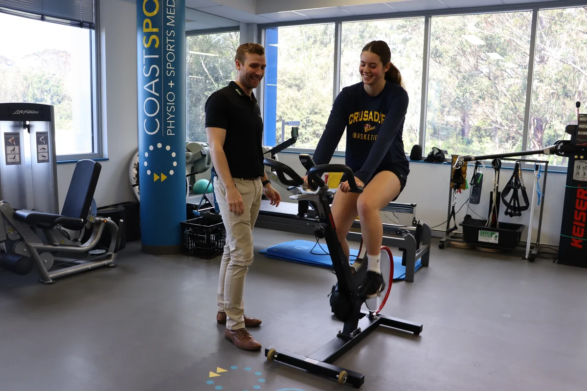Coast Sport practitioner supervising a client on a stationary bike for low impact cardio