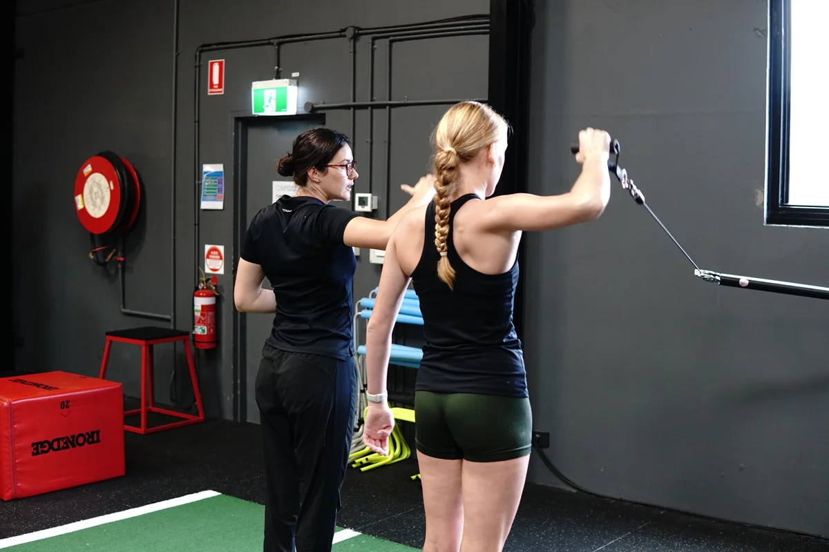 Coast Sport strength and conditioning coach cueing a client on a cable resistance exercise