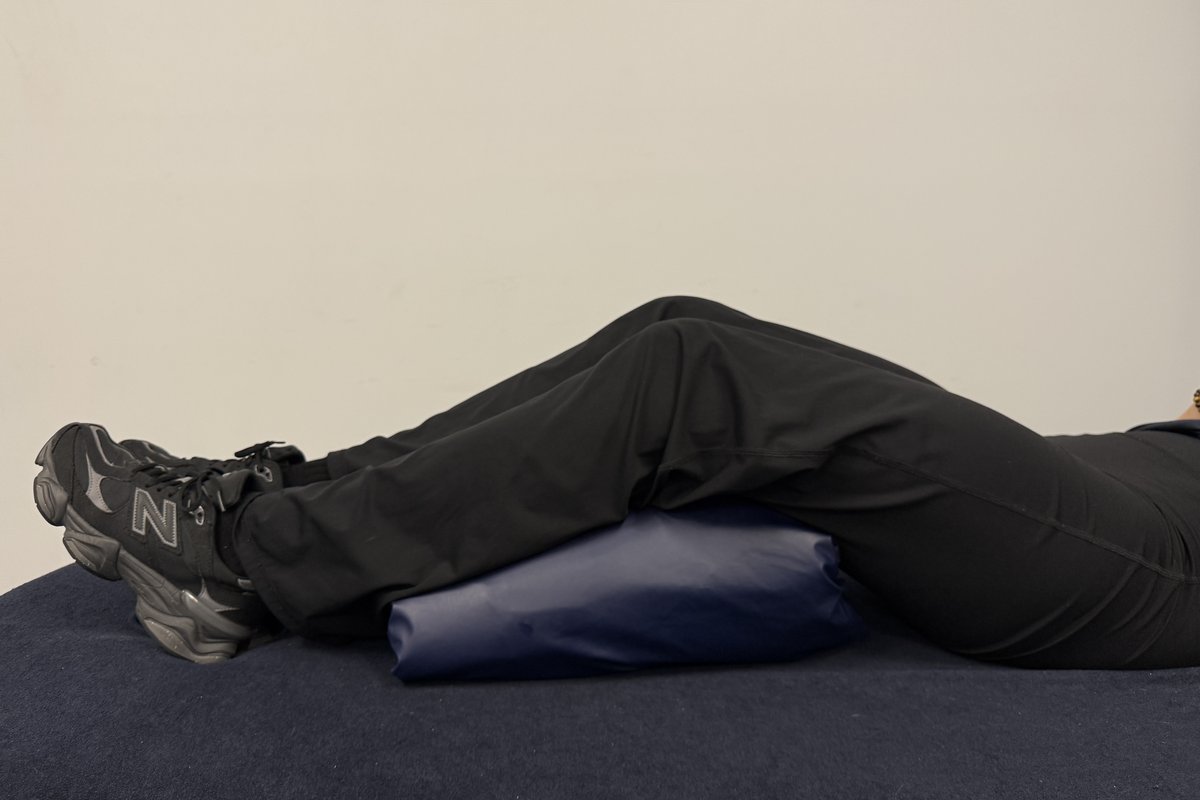 Person lying on their back with a pillow supporting under the knees
